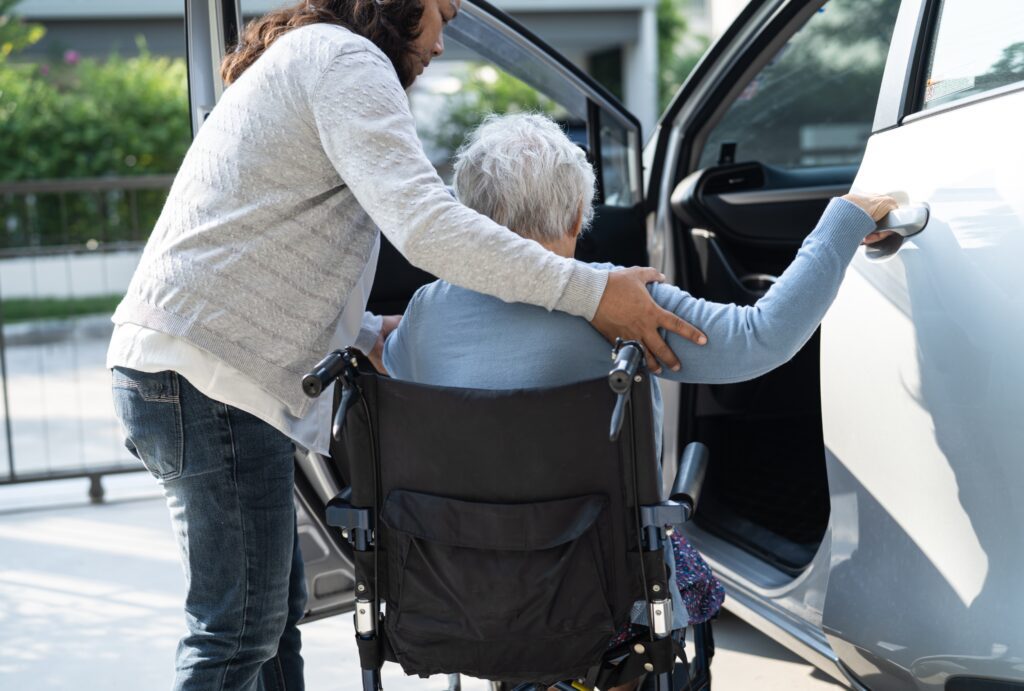 Care assistant guiding elderly woman into car